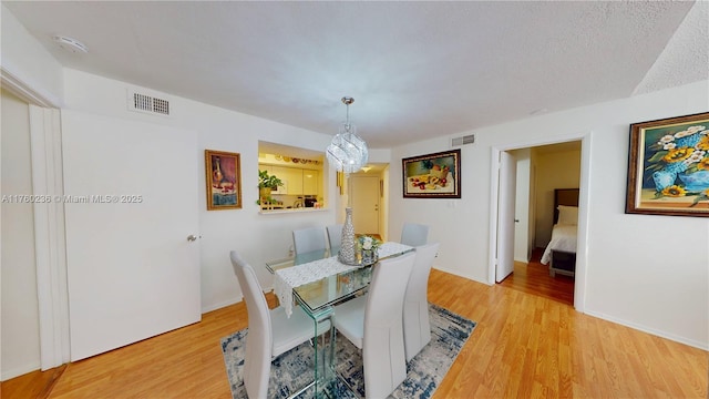 dining space featuring a textured ceiling, light wood-style floors, visible vents, and baseboards