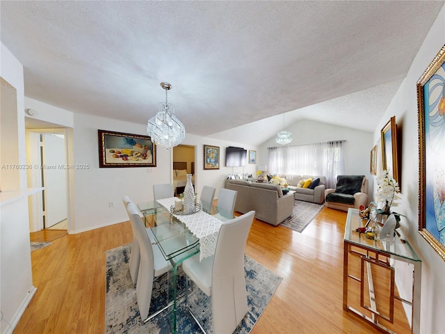 dining space with lofted ceiling, a notable chandelier, light wood-type flooring, and a textured ceiling