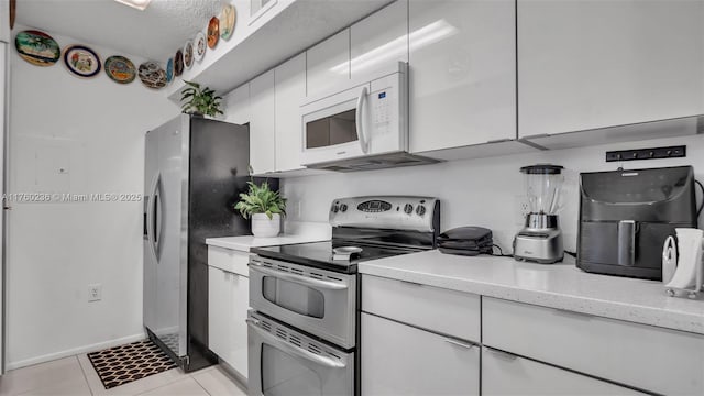 kitchen with baseboards, light stone countertops, light tile patterned floors, white cabinets, and stainless steel appliances