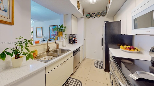 kitchen featuring light countertops, appliances with stainless steel finishes, light tile patterned flooring, white cabinets, and a sink