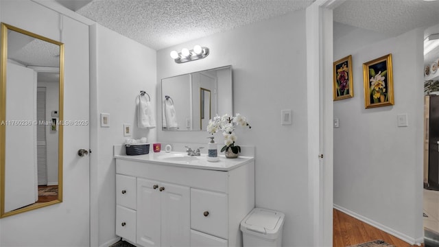 bathroom with vanity, wood finished floors, baseboards, and a textured ceiling