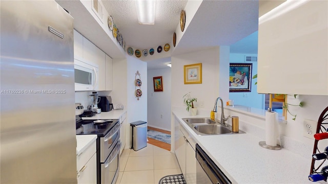 kitchen with a sink, appliances with stainless steel finishes, white cabinets, and light tile patterned floors