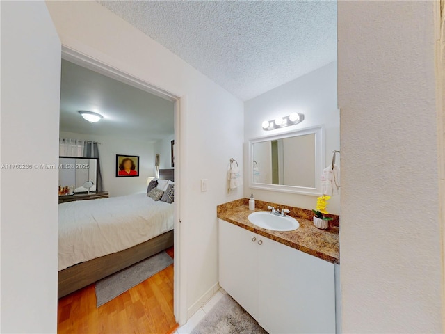 ensuite bathroom with connected bathroom, a textured ceiling, wood finished floors, and vanity