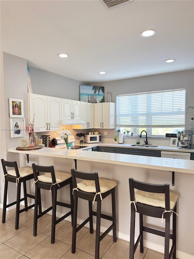 kitchen with white microwave, visible vents, a sink, white cabinets, and a kitchen breakfast bar