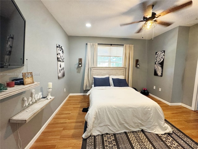 bedroom with ceiling fan, baseboards, a textured ceiling, and light wood-style flooring