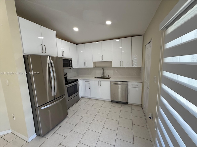 kitchen with a sink, light tile patterned floors, stainless steel appliances, light countertops, and white cabinetry