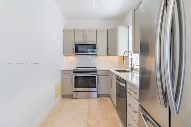 kitchen with gray cabinetry, a sink, light countertops, appliances with stainless steel finishes, and backsplash