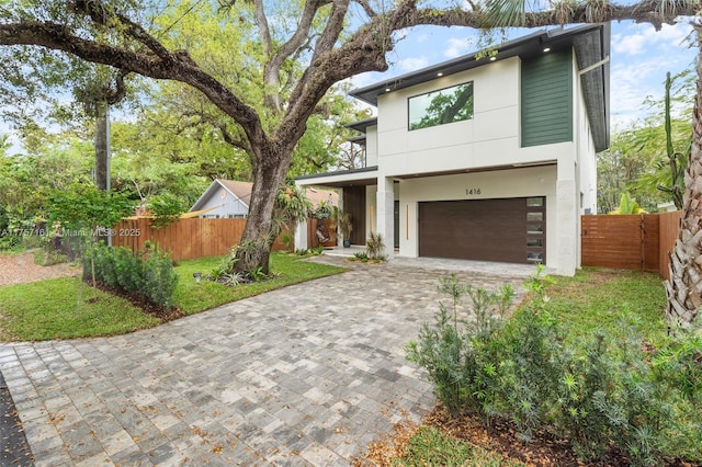 modern home with a balcony, fence, an attached garage, stucco siding, and decorative driveway