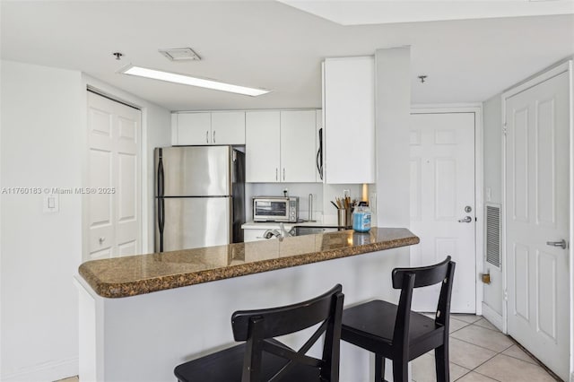 kitchen featuring a kitchen breakfast bar, stainless steel appliances, a peninsula, light tile patterned flooring, and white cabinetry