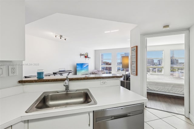 kitchen featuring white cabinetry, light tile patterned flooring, a sink, stainless steel dishwasher, and open floor plan