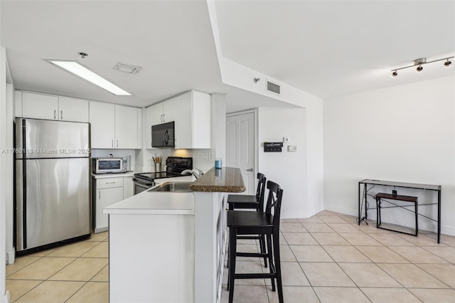 kitchen featuring electric stove, freestanding refrigerator, a peninsula, black microwave, and light tile patterned floors