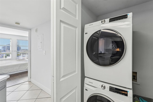 laundry room featuring light tile patterned floors, stacked washer / drying machine, baseboards, and laundry area