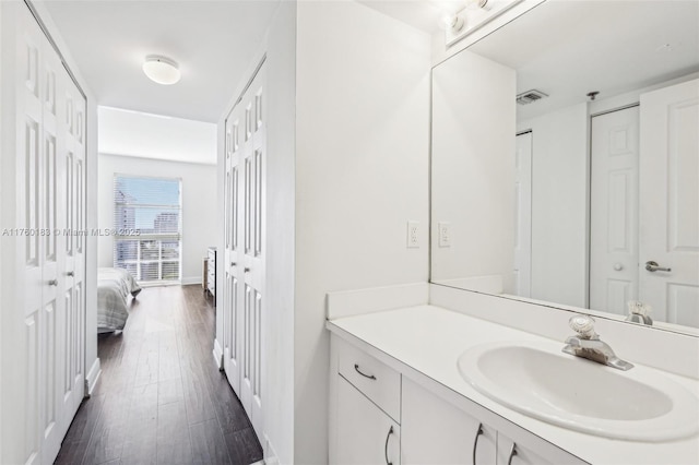 ensuite bathroom with connected bathroom, visible vents, wood finished floors, and vanity