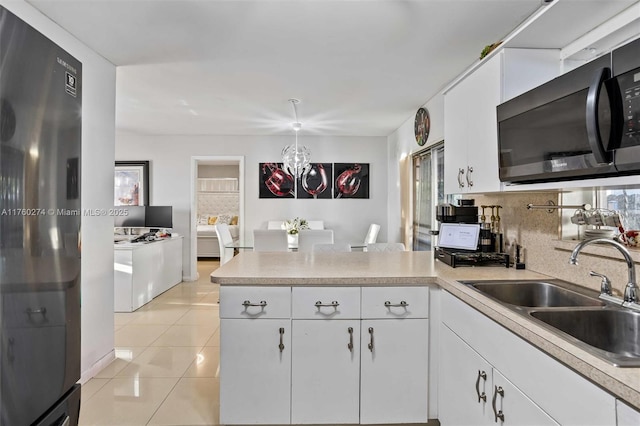 kitchen with light countertops, decorative backsplash, a peninsula, fridge, and a sink