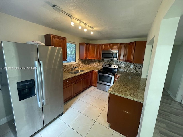 kitchen featuring stone counters, a sink, decorative backsplash, stainless steel appliances, and a textured ceiling