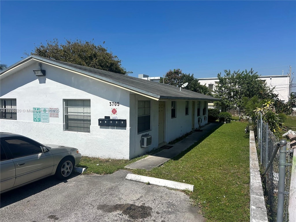 view of side of property with uncovered parking, a lawn, fence, and stucco siding