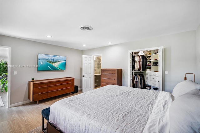 bedroom with a walk in closet, light wood-style floors, recessed lighting, baseboards, and visible vents