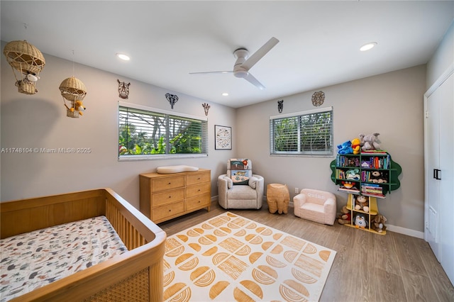 bedroom featuring recessed lighting, a nursery area, wood finished floors, and a ceiling fan