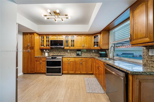 kitchen with dark stone countertops, brown cabinetry, light wood finished floors, a sink, and stainless steel appliances