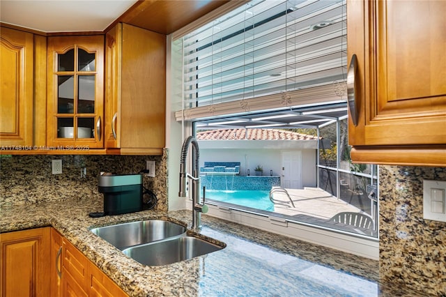 kitchen featuring tasteful backsplash, brown cabinets, glass insert cabinets, and a sink