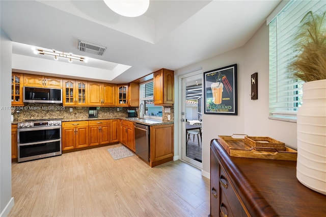 kitchen featuring brown cabinets, appliances with stainless steel finishes, a raised ceiling, light wood-style floors, and visible vents