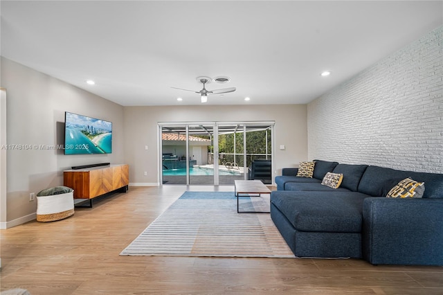 living room with brick wall, an accent wall, ceiling fan, baseboards, and wood finished floors