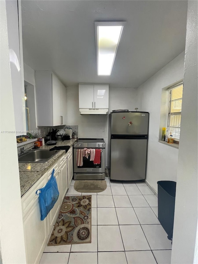kitchen with under cabinet range hood, a sink, white cabinetry, appliances with stainless steel finishes, and light tile patterned floors