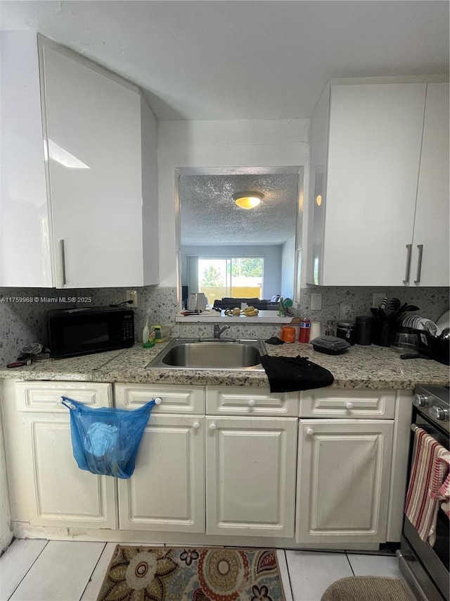 kitchen featuring black microwave, light tile patterned floors, stove, white cabinets, and a textured ceiling