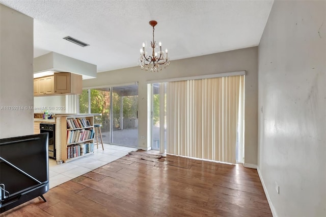 interior space featuring light wood finished floors, visible vents, baseboards, an inviting chandelier, and a textured ceiling