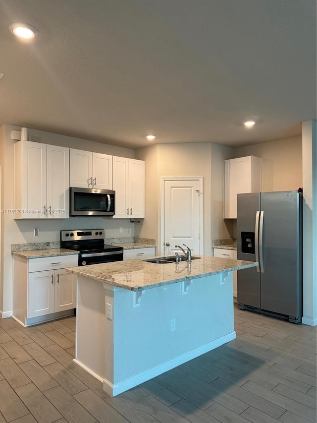 kitchen with light wood-style flooring, a sink, stainless steel appliances, white cabinets, and light stone countertops