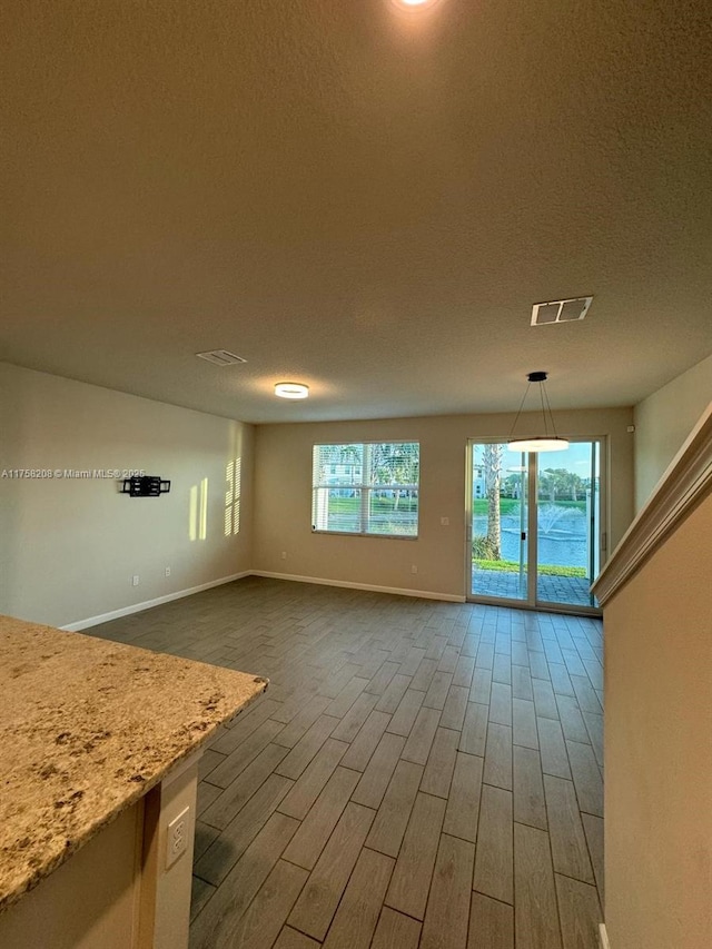 unfurnished living room with visible vents, baseboards, a textured ceiling, and dark wood-style flooring