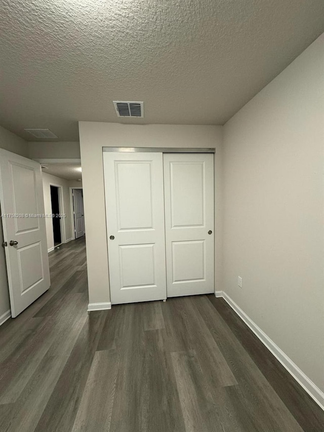 unfurnished bedroom with visible vents, baseboards, a closet, and dark wood-style floors