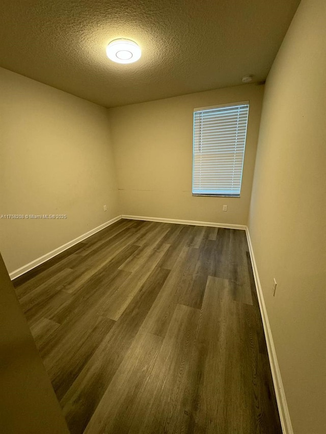 unfurnished room featuring baseboards, a textured ceiling, and dark wood-style floors