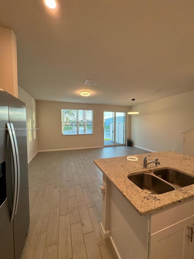 kitchen featuring light stone counters, light wood-style flooring, stainless steel fridge with ice dispenser, a sink, and open floor plan