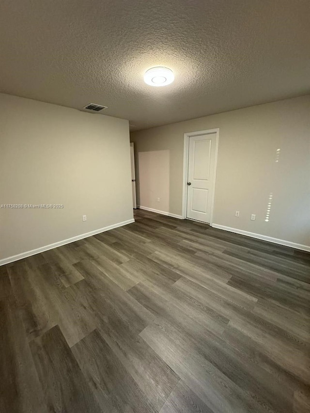 spare room with visible vents, baseboards, dark wood-type flooring, and a textured ceiling