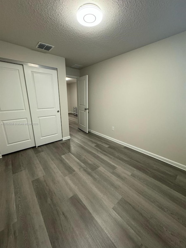 unfurnished bedroom featuring visible vents, baseboards, a closet, and dark wood-style floors