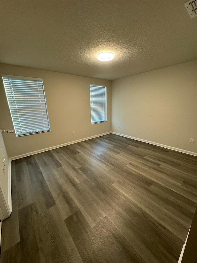 spare room with visible vents, a textured ceiling, baseboards, and dark wood-style flooring