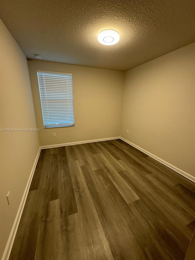 empty room featuring a textured ceiling, baseboards, and dark wood-style flooring