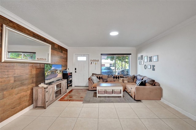 living room featuring light tile patterned floors, baseboards, ornamental molding, wood walls, and a textured ceiling