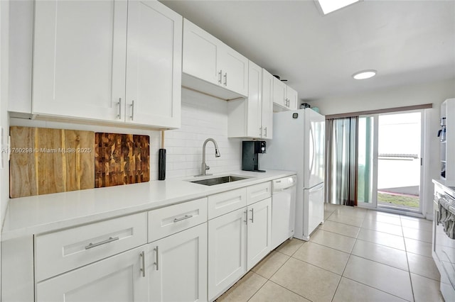 kitchen featuring white appliances, light tile patterned floors, a sink, decorative backsplash, and white cabinets