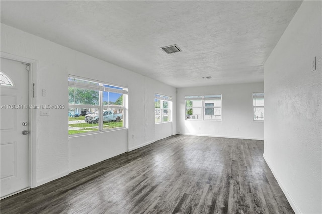 empty room with visible vents, a textured ceiling, a textured wall, and wood finished floors