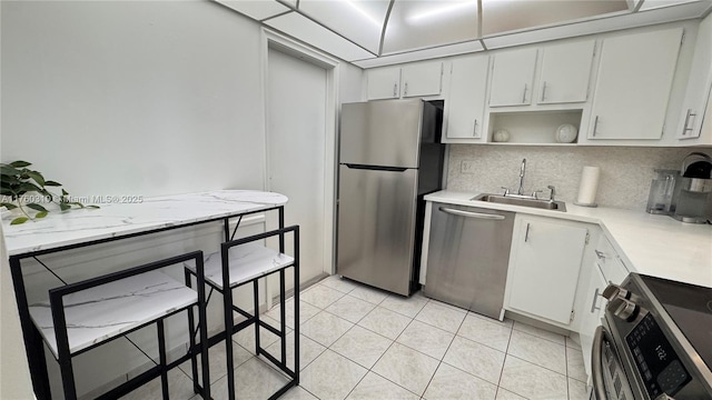 kitchen featuring a sink, light countertops, decorative backsplash, appliances with stainless steel finishes, and open shelves