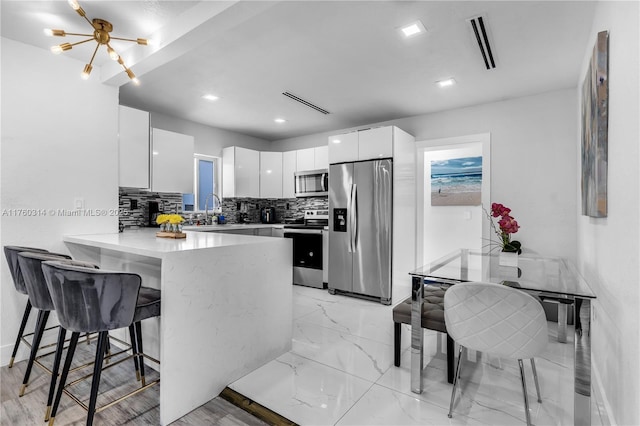 231 NW 44th St, Miami, FL 33127 - kitchen featuring appliances with stainless steel finishes, a peninsula, white cabinetry, decorative backsplash, and a breakfast bar area