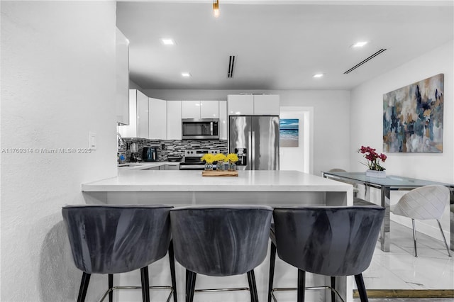231 NW 44th St, Miami, FL 33127 - kitchen with stainless steel appliances, light countertops, white cabinetry, a peninsula, and a breakfast bar area