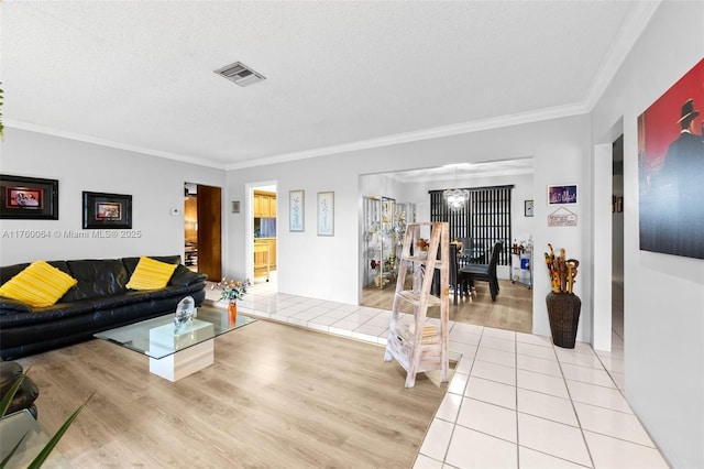 living area featuring light tile patterned flooring, visible vents, a textured ceiling, and ornamental molding