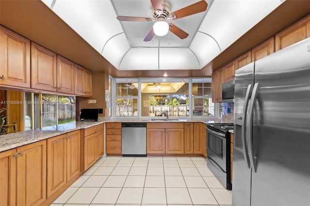 kitchen with light stone counters, light tile patterned flooring, a sink, stainless steel appliances, and vaulted ceiling