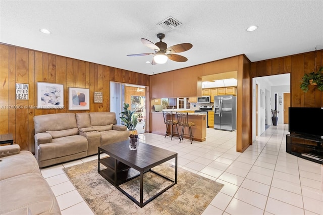 living room featuring visible vents, wooden walls, light tile patterned floors, a textured ceiling, and a ceiling fan