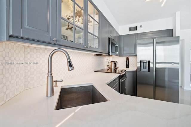 kitchen featuring visible vents, gray cabinets, tasteful backsplash, stainless steel appliances, and glass insert cabinets