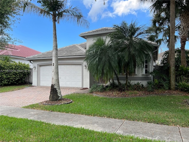 view of front facade with a front yard, stucco siding, a garage, a tile roof, and decorative driveway