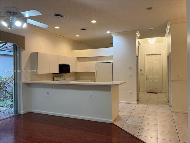 kitchen with visible vents, black microwave, light countertops, a peninsula, and freestanding refrigerator